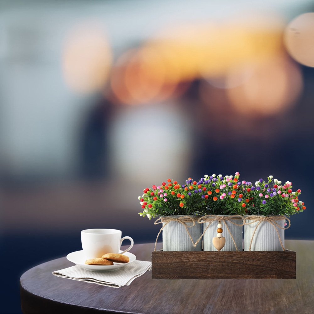 Artificial flower centerpiece set with three metal pots on a wooden tray, next to a coffee cup and cookies.