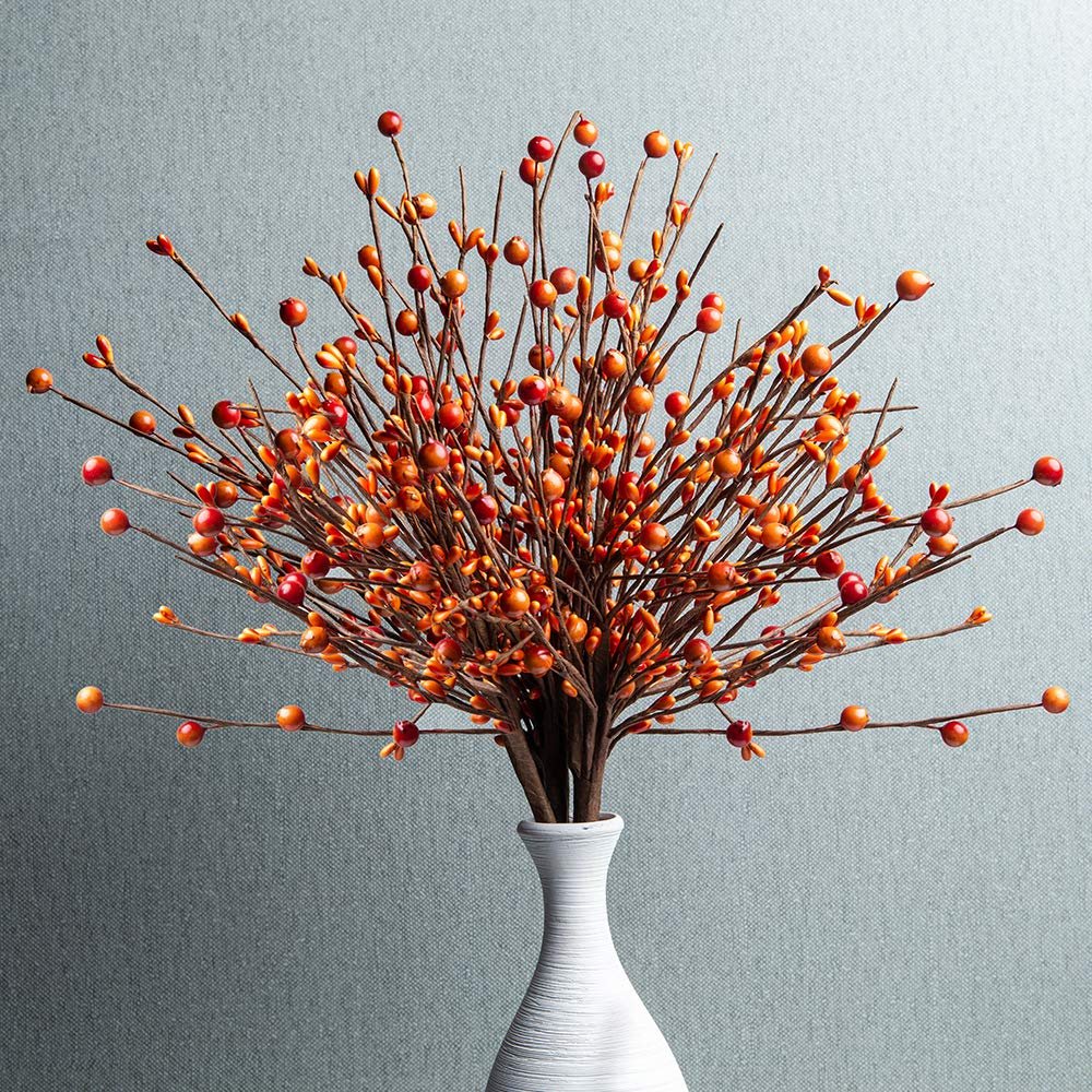 Artificial orange berry stems in a white vase against a textured gray background.