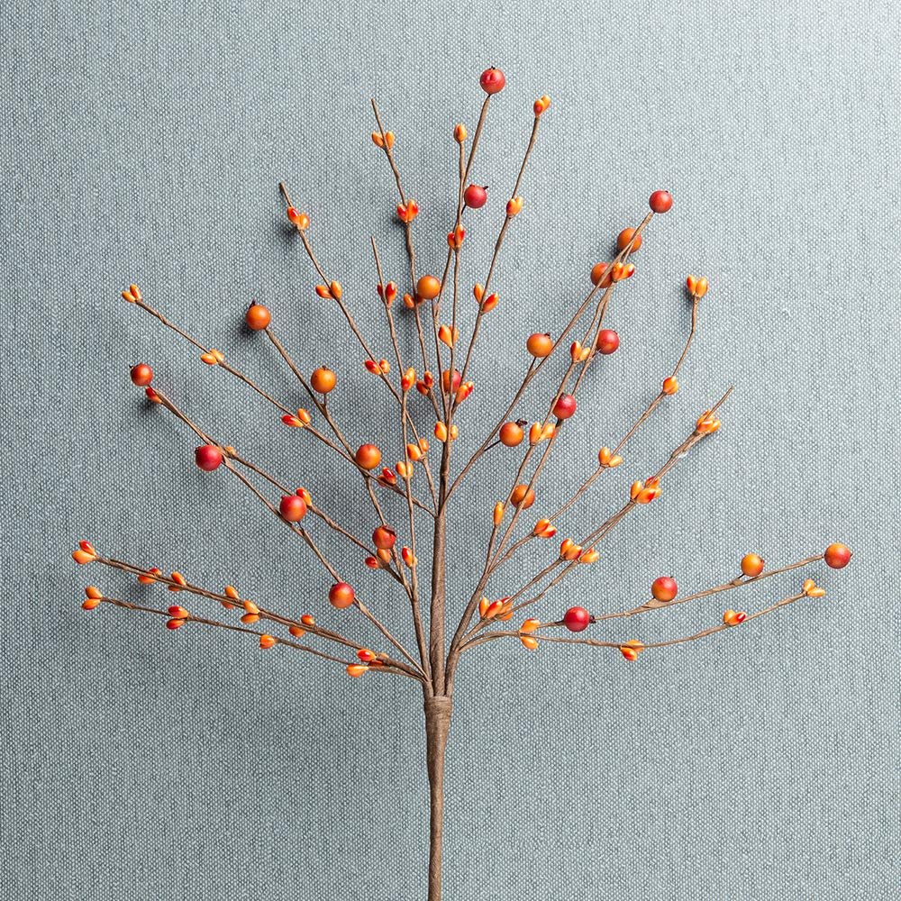 Artificial orange berry pick with red and orange berries on a gray textured background.