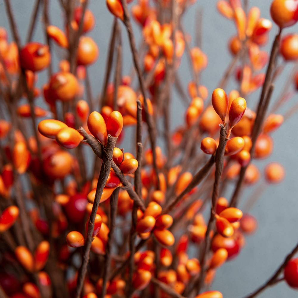 Close-up of artificial orange berry stems with brown branches against a gray background.