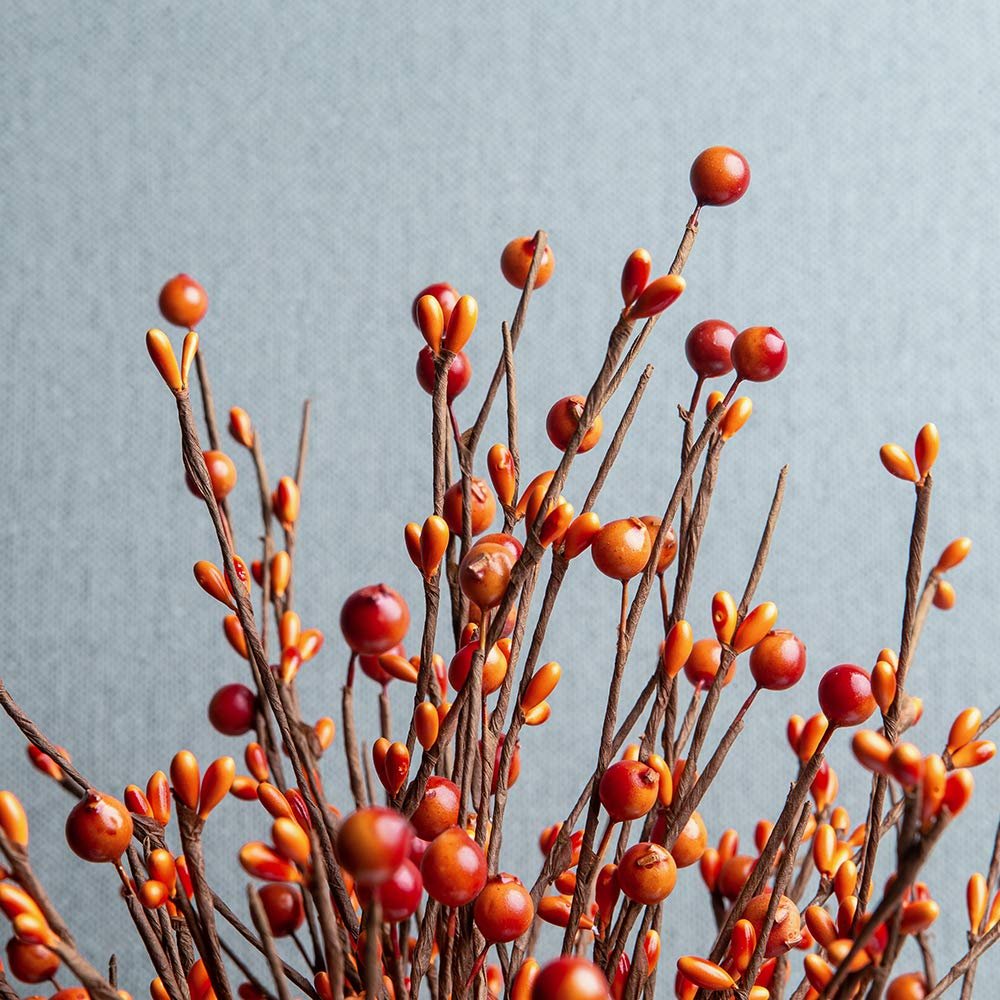 Close-up of artificial orange berry stems with red berries and small buds against a gray background.