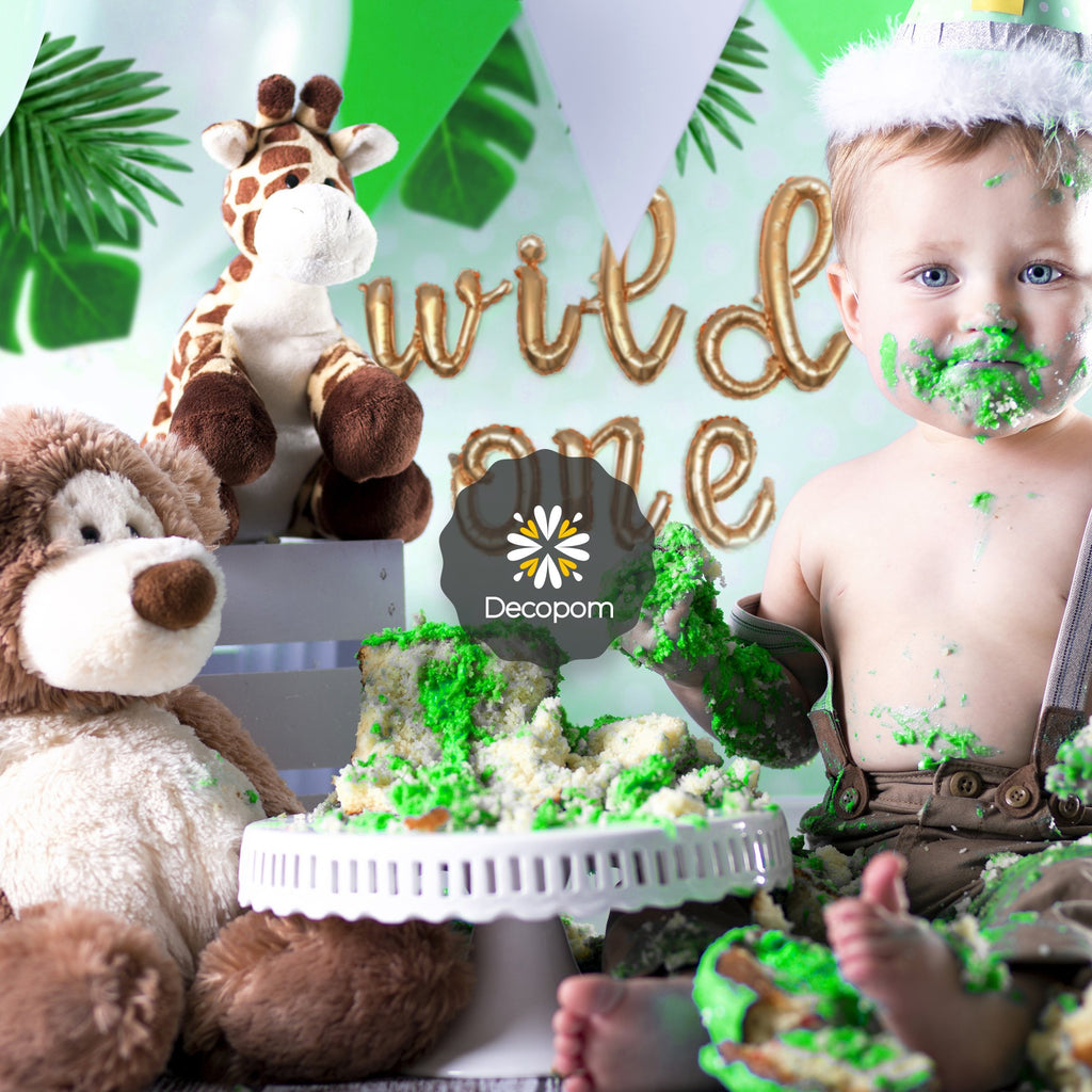 Baby covered in cake with stuffed animals and 'wild one' balloons in background