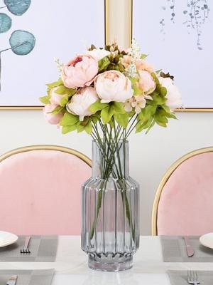 Light pink artificial peony bouquet in a ribbed glass vase on a table with pink chairs in the background.