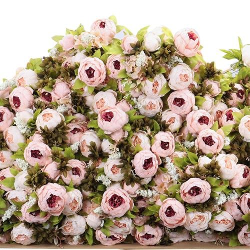 A dense pile of light pink artificial peony flowers with green leaves and small white accents, viewed from a slightly elevated angle.