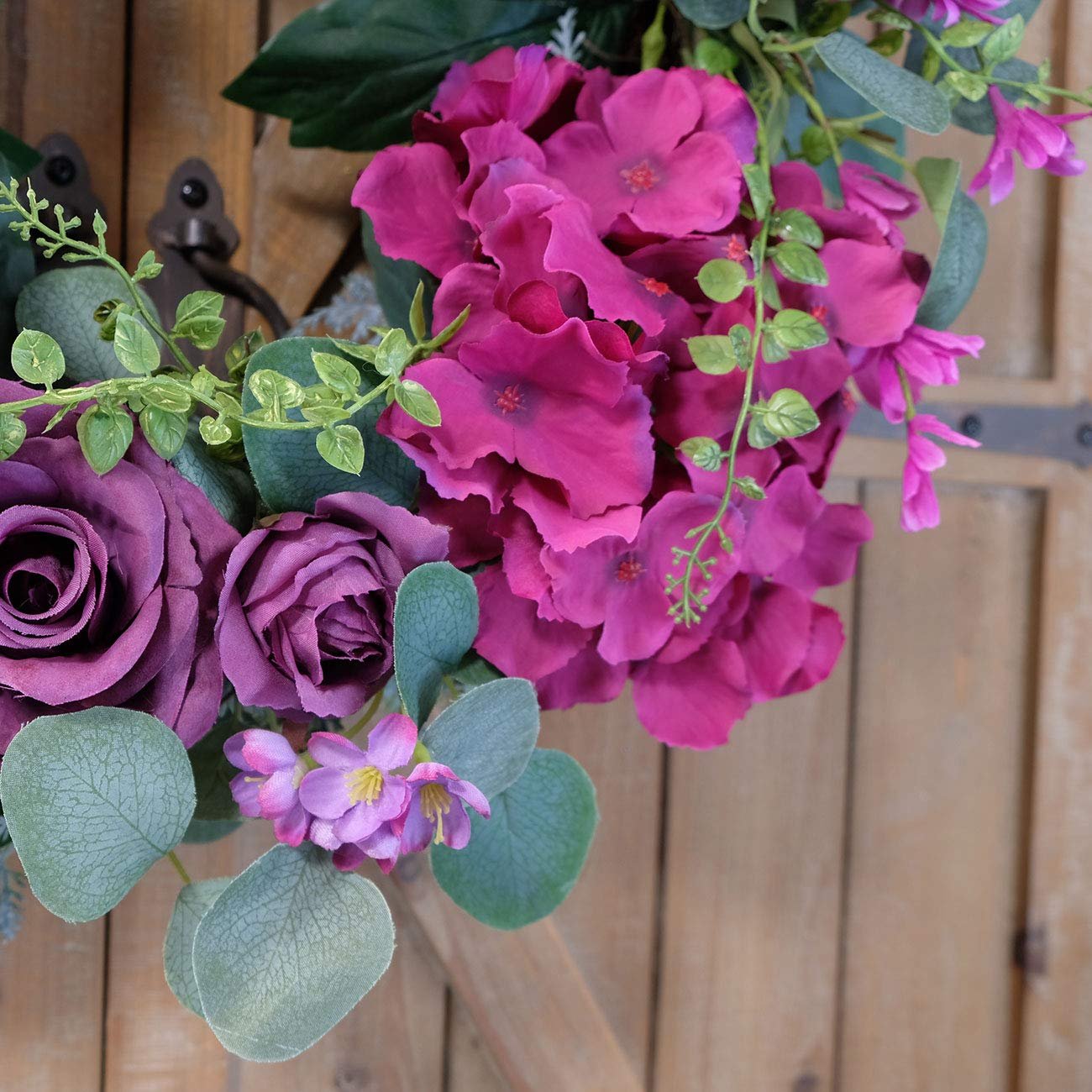 Close-up of a purple rose and hydrangea artificial wreath with eucalyptus leaves on a wooden background.