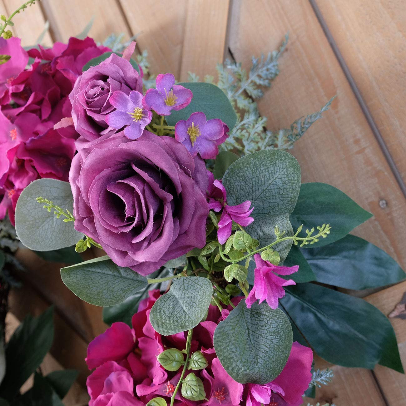 Close-up of a purple rose wreath with silk hydrangea and eucalyptus leaves on a wooden background.