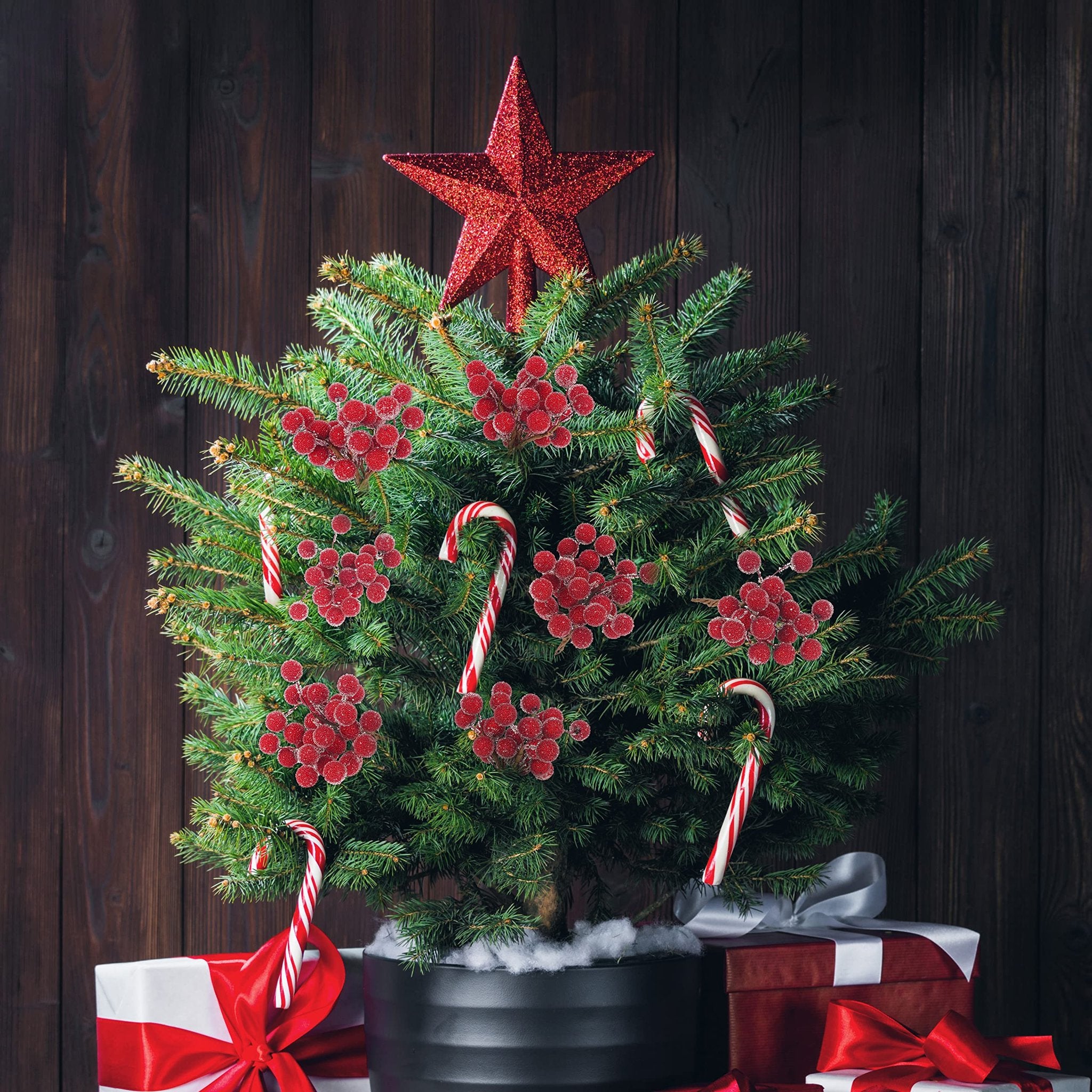 Christmas tree decorated with red berry picks and candy canes, with gifts at its base.