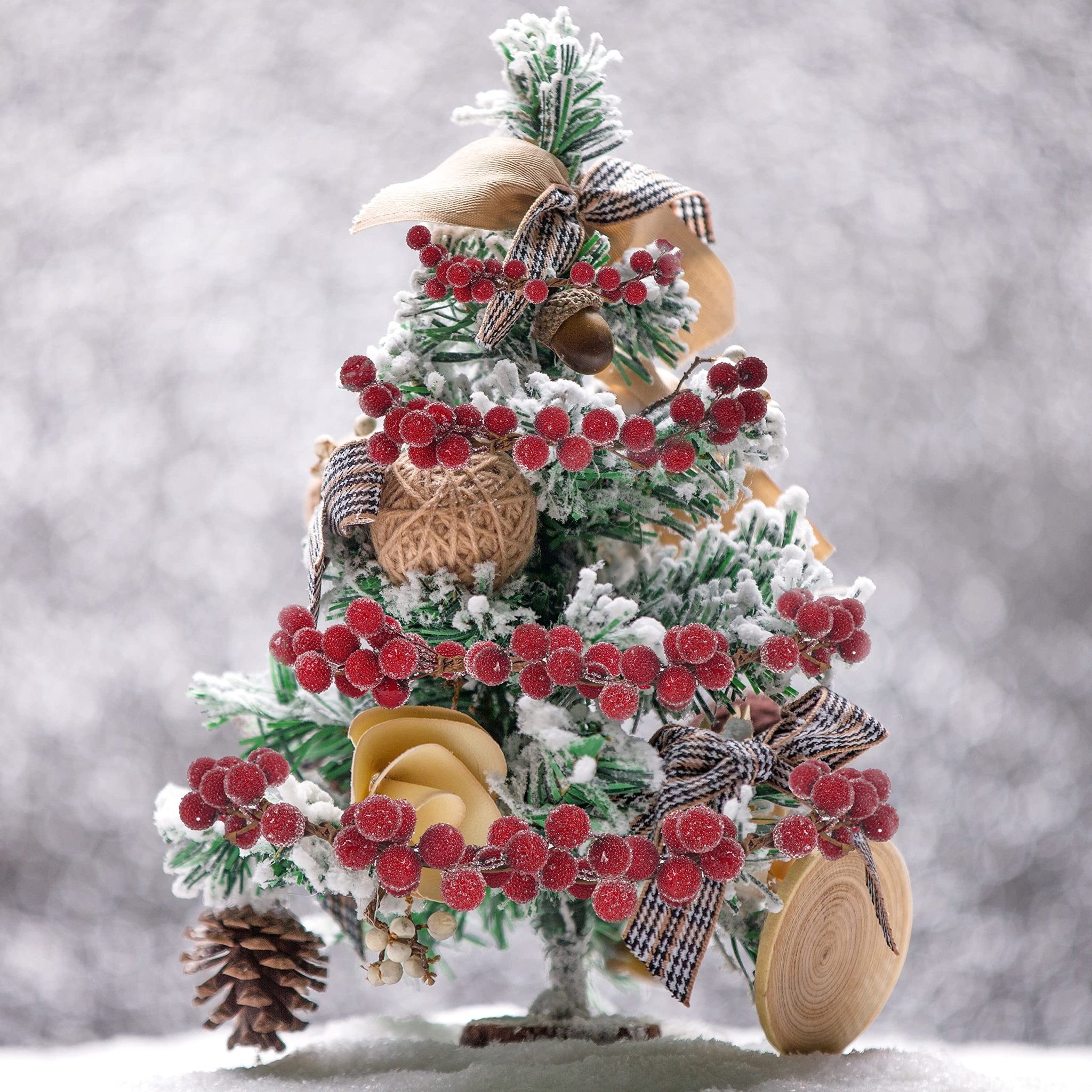 Frosted artificial Christmas tree decorated with red holly berries, pinecones, and bows.