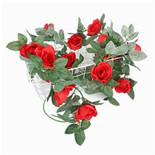 Red artificial rose vine garland with green leaves draped over a white wire basket.