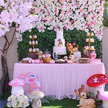 Woodland themed party table with cake, cupcakes, and Bambi decorations, set against a floral backdrop.