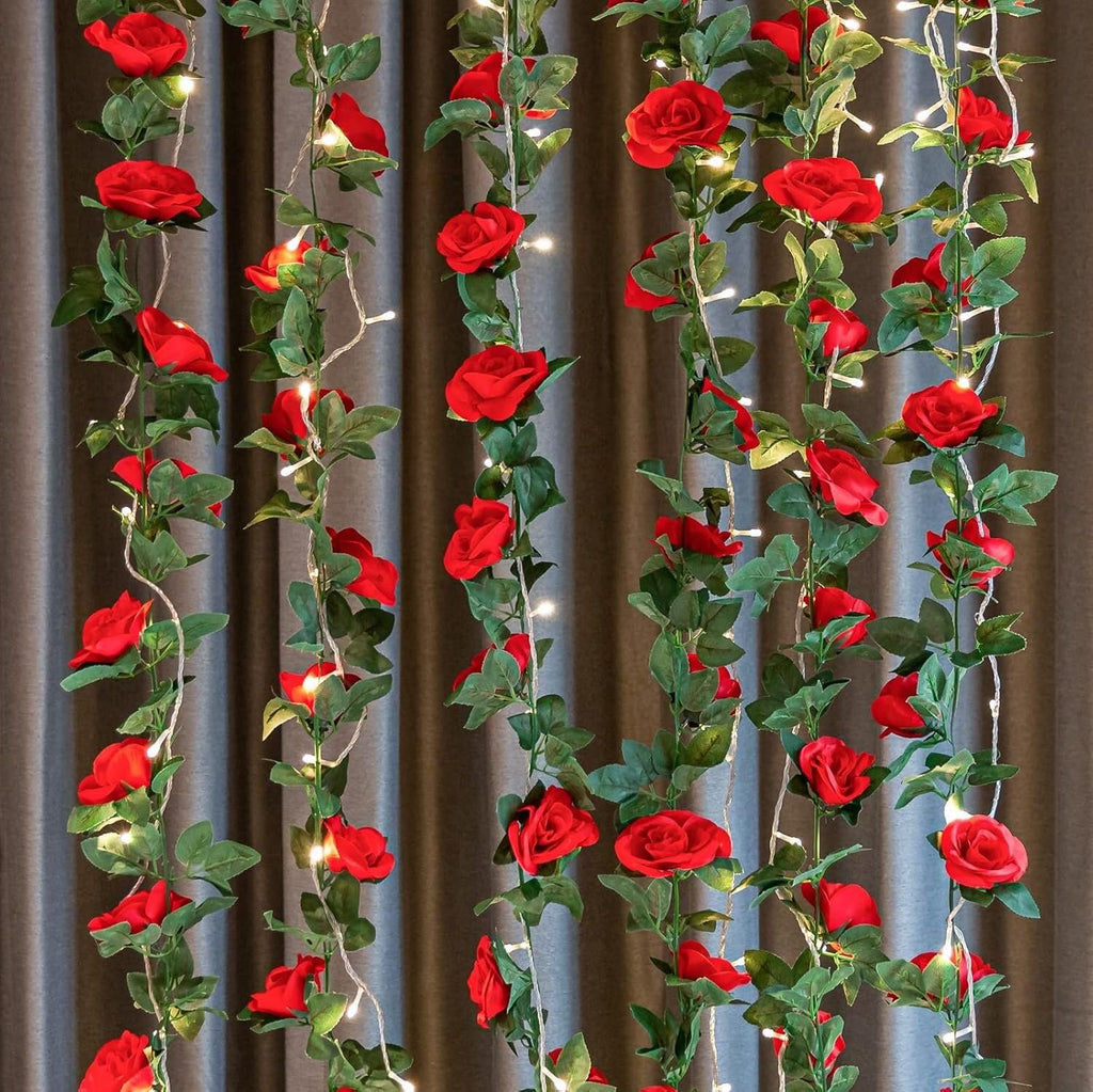 Artificial red rose vine garland with LED string lights draped against a grey curtain background.