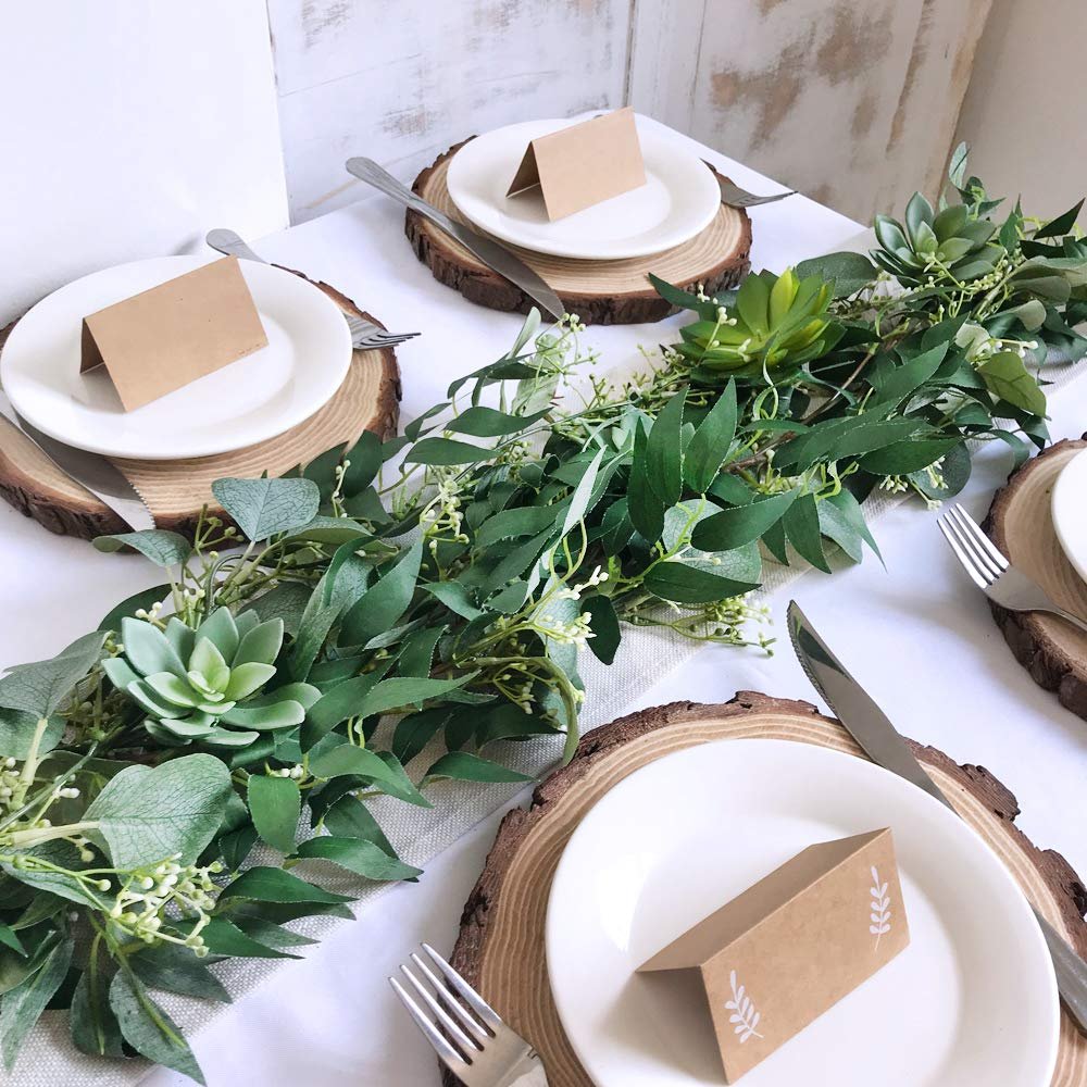 Artificial eucalyptus and willow twig garland draped across a table setting with plates, wood slices, and place cards.
