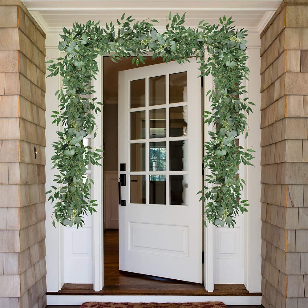 Artificial eucalyptus and willow twig garland draped over an open doorway on a shingled house exterior.