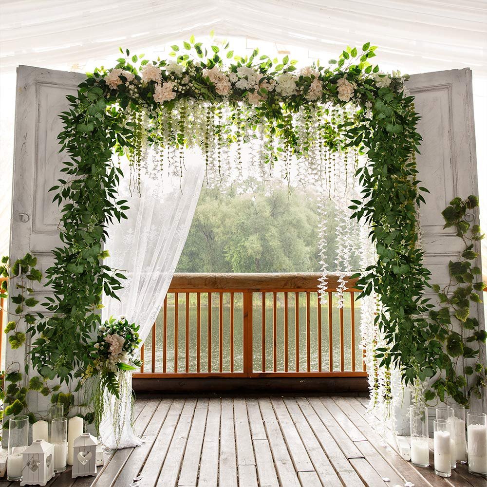 Artificial eucalyptus and willow twig garland draped over an archway with flowers and hanging white blossoms.