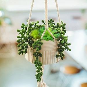 Artificial succulent plants in a cream-colored pot hanging from a macrame hanger, with a blurred background.