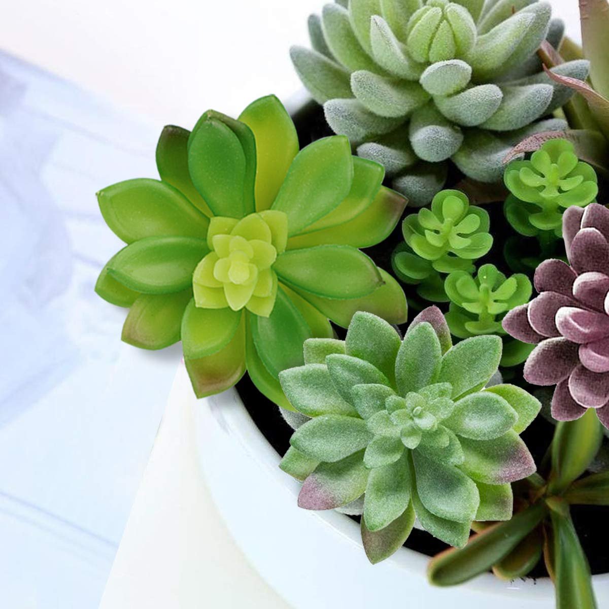 Close-up of a variety of unpotted artificial succulent plants in shades of green and purple, arranged in a white pot.