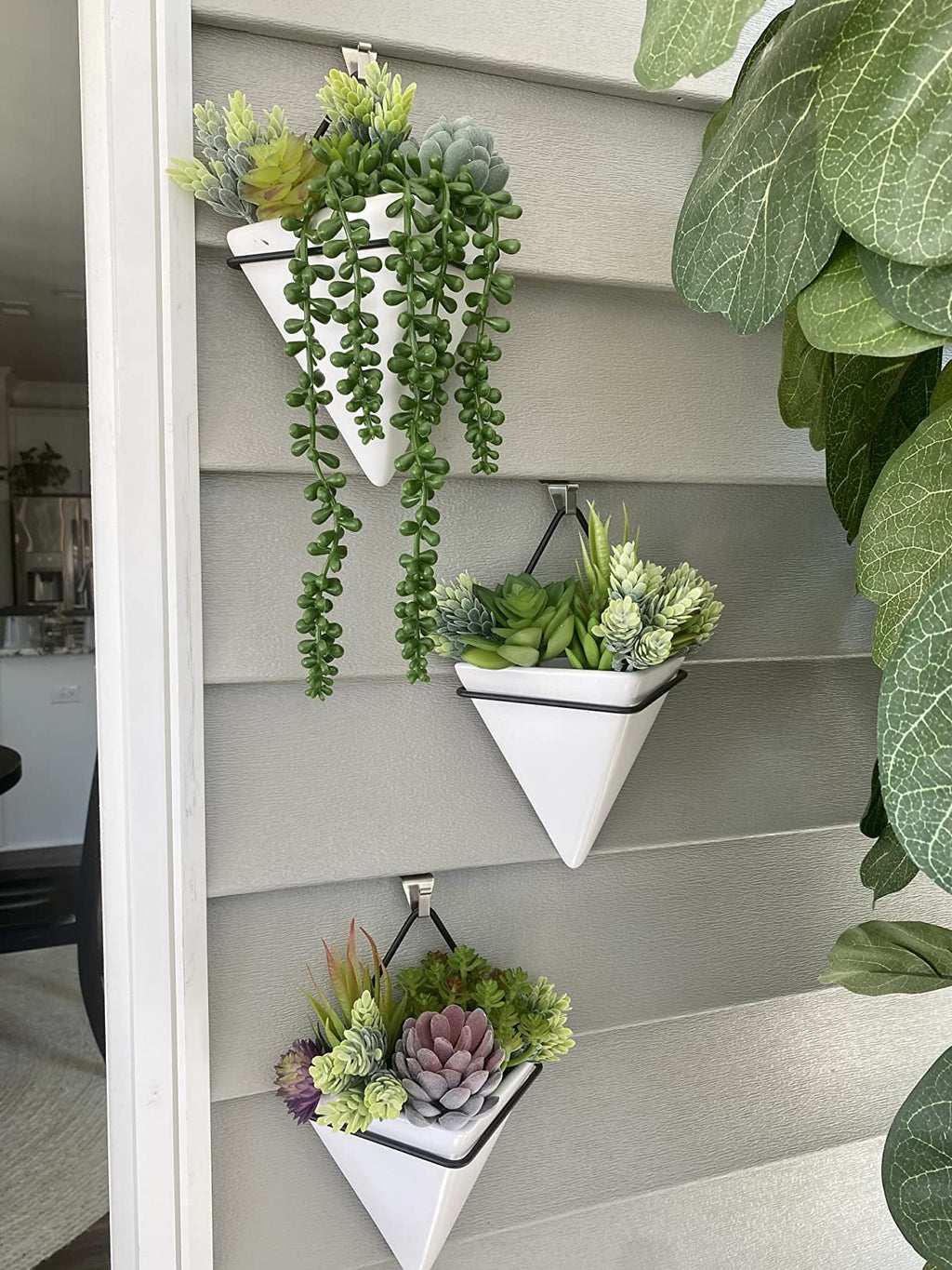 Three white triangular planters with artificial succulents hanging on a gray wall