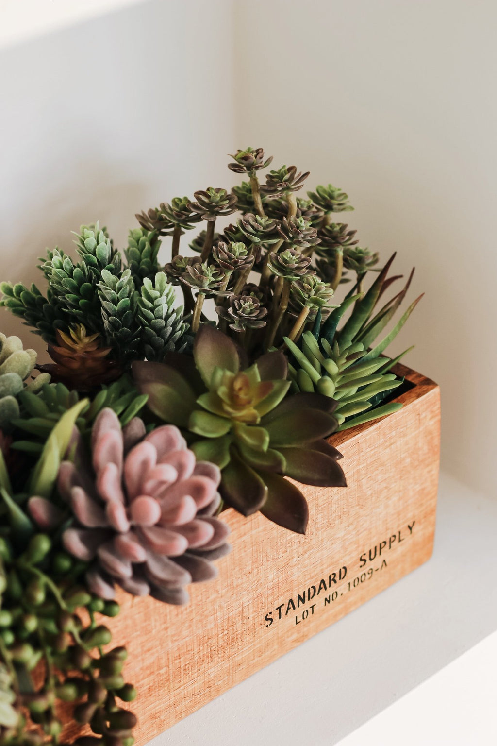 Assorted artificial succulents in a wooden planter box with visible text.