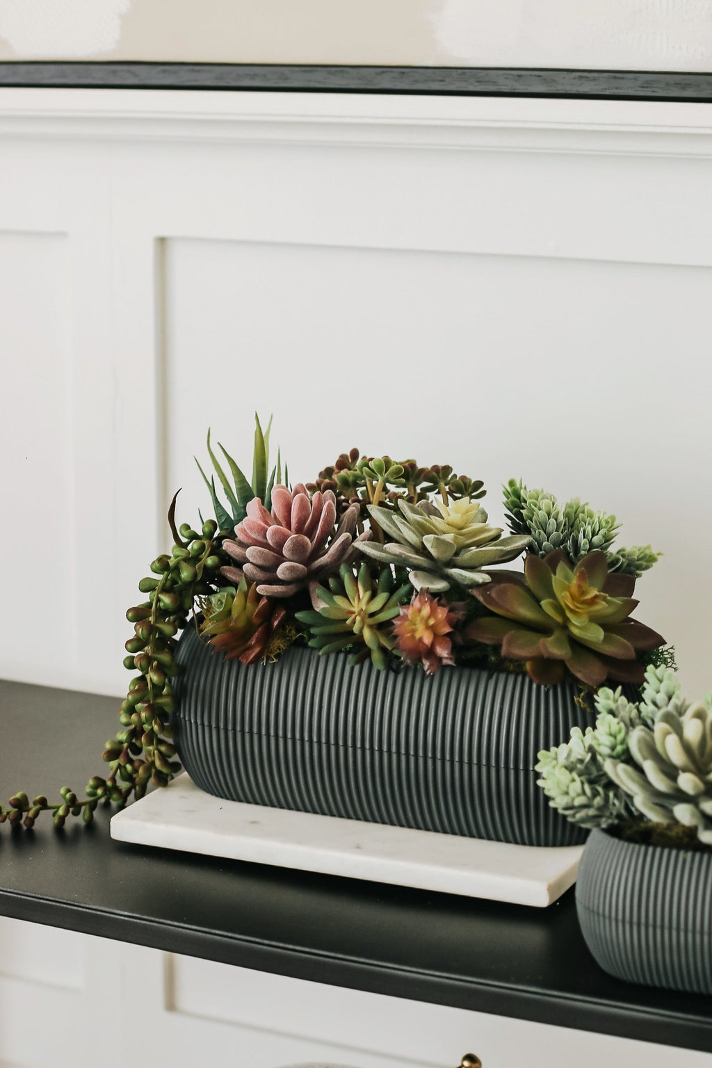 Assorted artificial succulents in a ribbed dark gray planter on a marble slab.