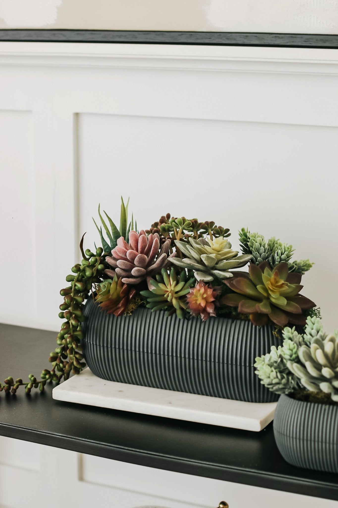 Assorted artificial succulents in a ribbed dark gray planter on a marble slab.