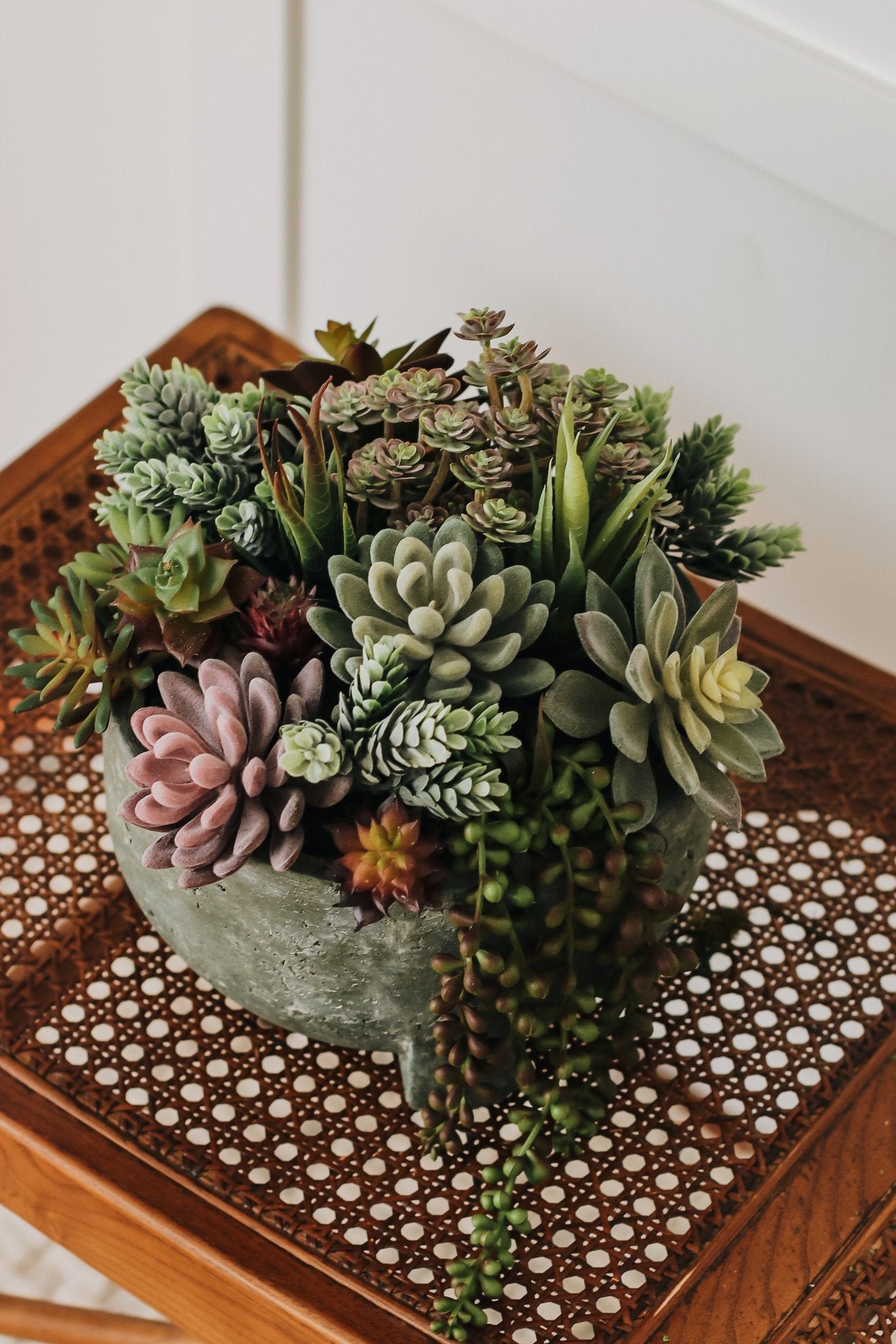 Assorted artificial succulents in a textured gray pot on a woven wooden surface.