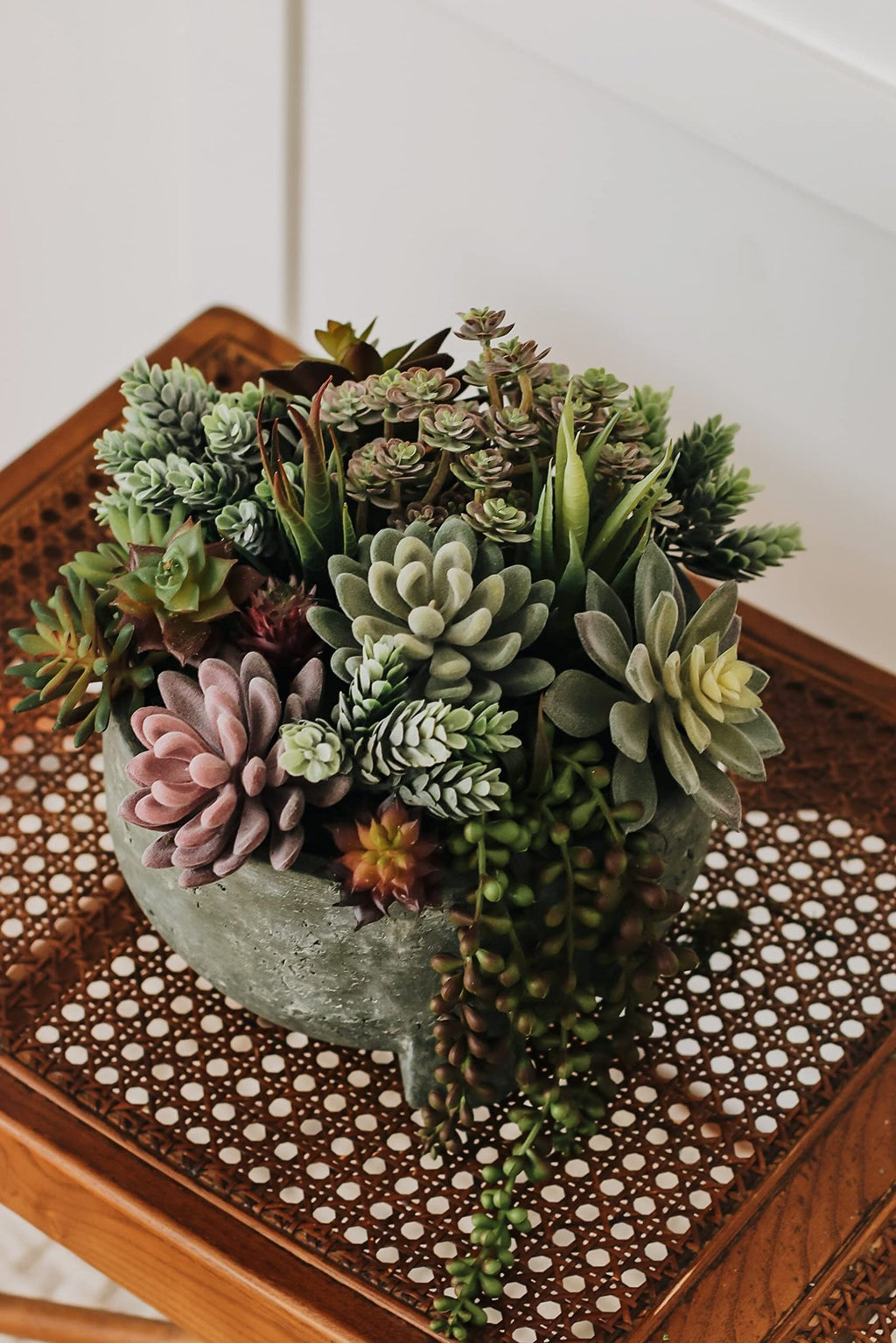 Assorted artificial succulents in a textured gray pot on a woven wooden surface.