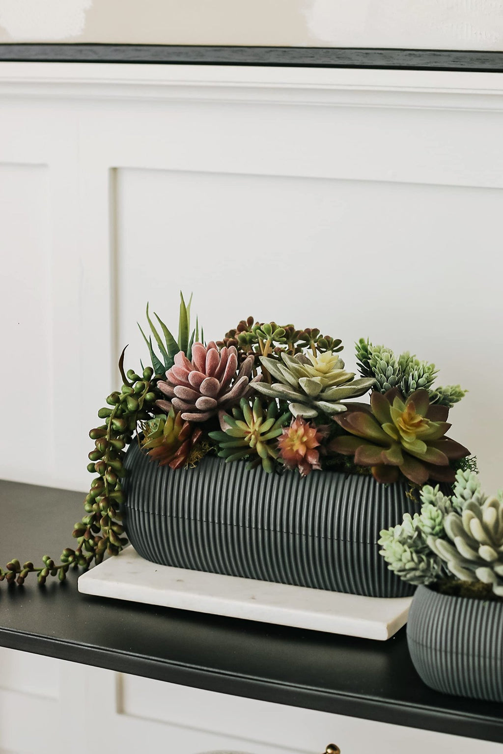 Assorted artificial succulents in a ribbed dark gray planter on a marble slab.