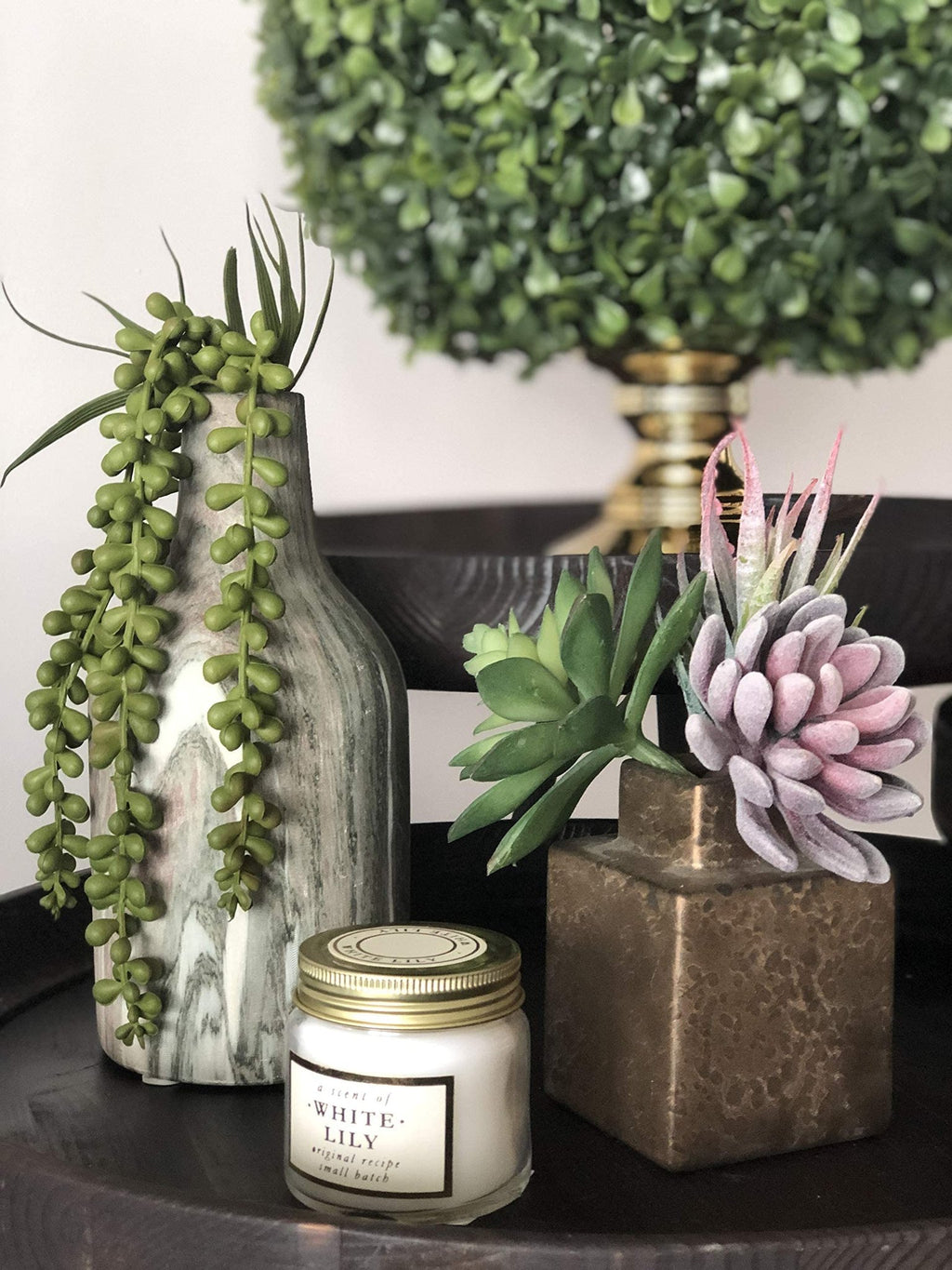 Assorted artificial succulents in decorative vases and a candle on a dark tray