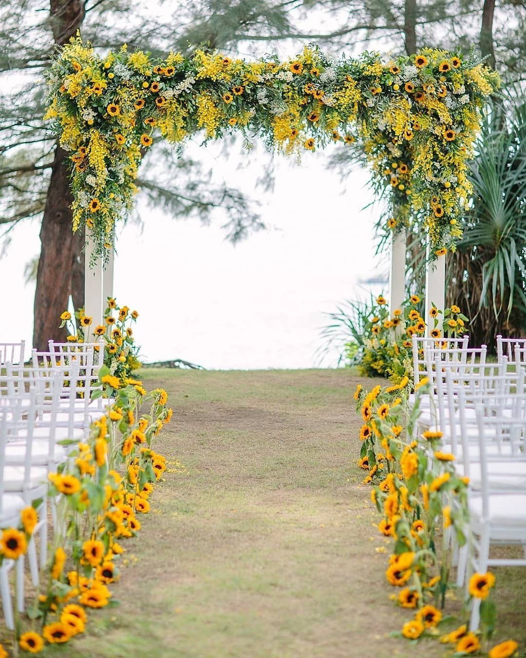 Wedding aisle decorated with artificial sunflower garland and white chairs on either side, leading to an archway.