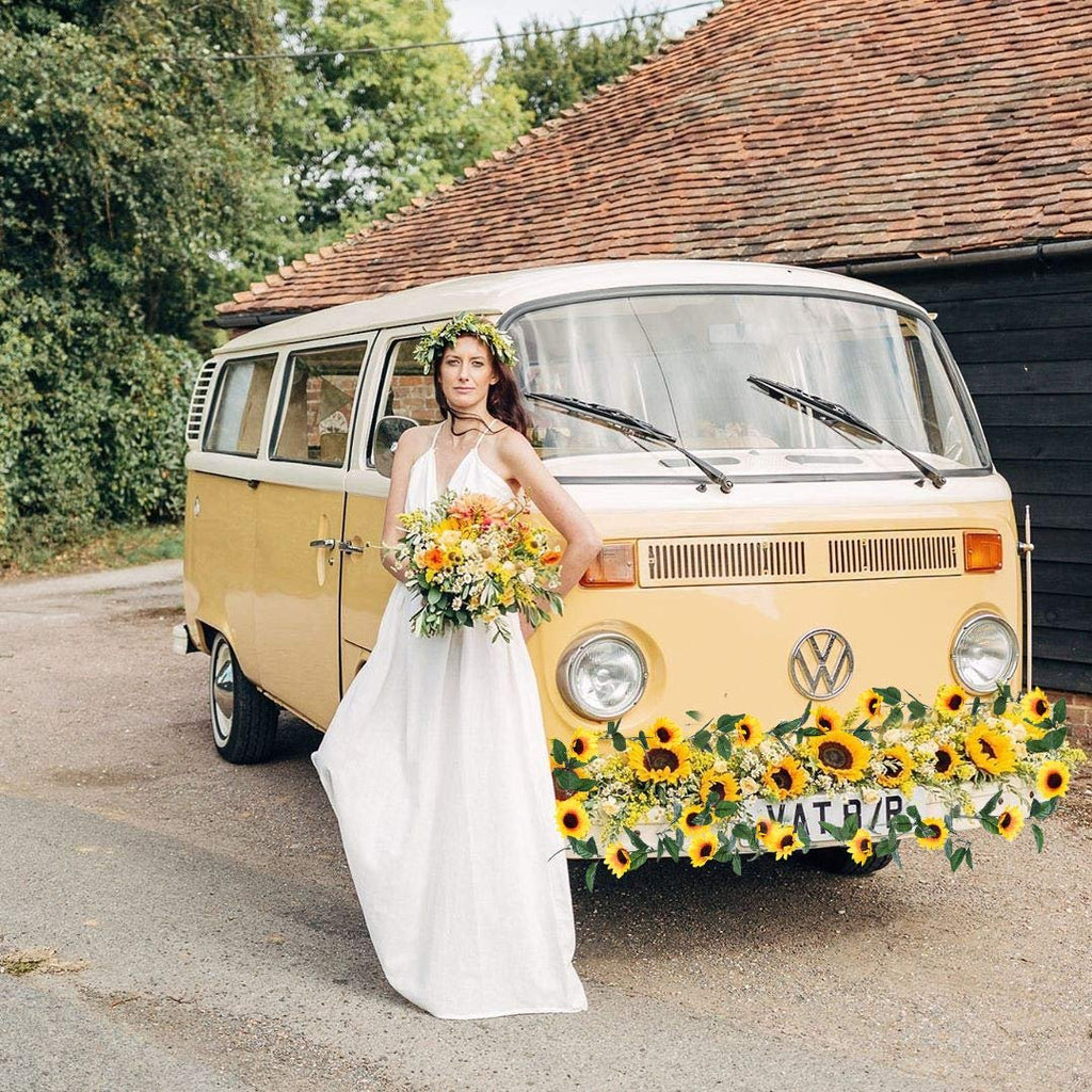 Bride in white dress holding bouquet poses with yellow van decorated with sunflowers