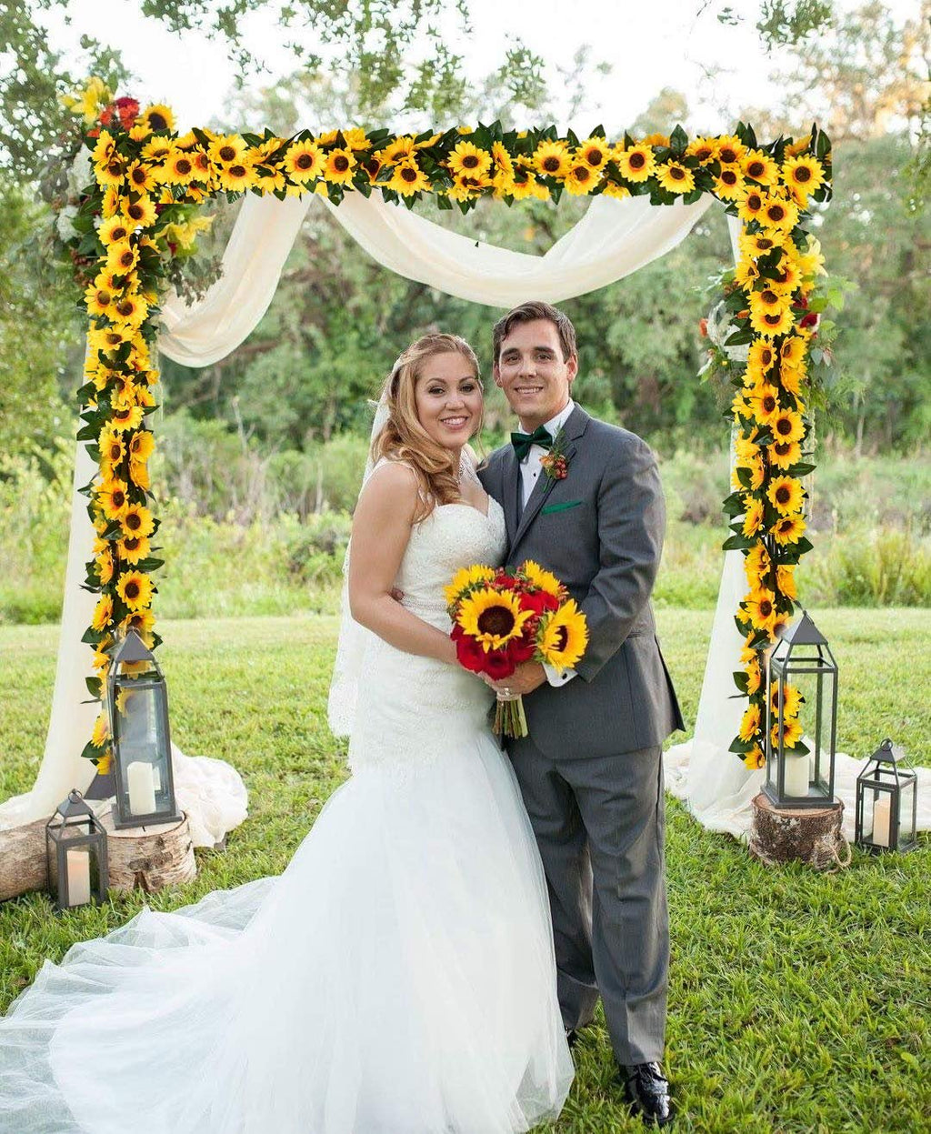 Bride and groom posing under a sunflower wedding arch decorated with white drapery and lanterns