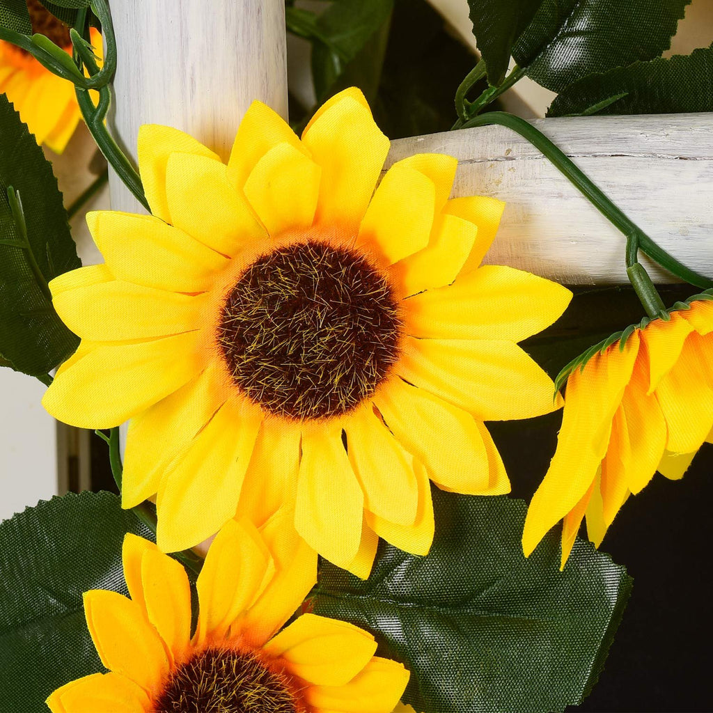 Artificial sunflower garland with green leaves draped over a white wooden surface.