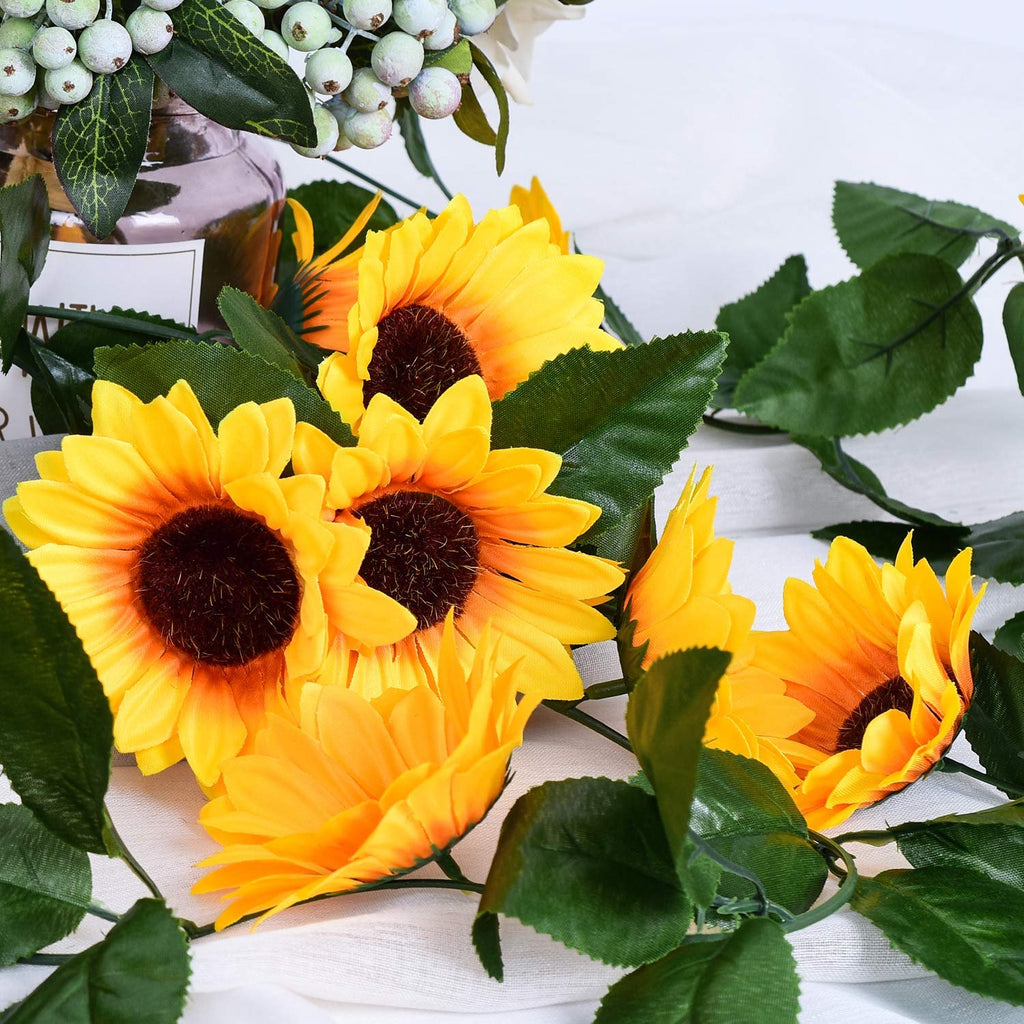 Artificial sunflower garland with green leaves and white berries in a glass jar, close-up view.