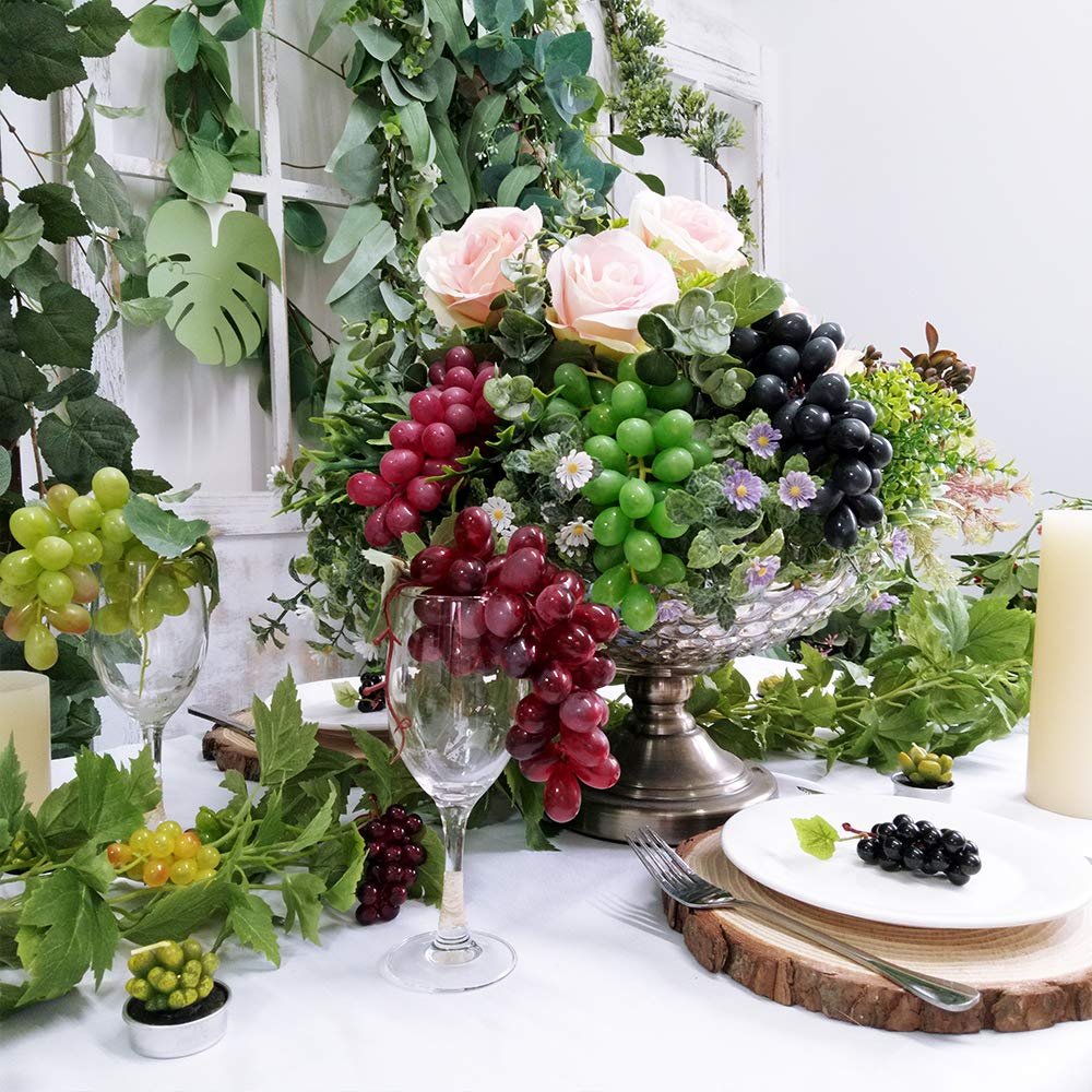 Assorted artificial grape clusters in a decorative arrangement with roses and greenery, set on a table.