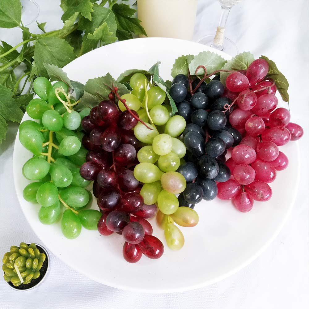 Assorted frosted artificial grape clusters in five colors on a white plate with green leaves.