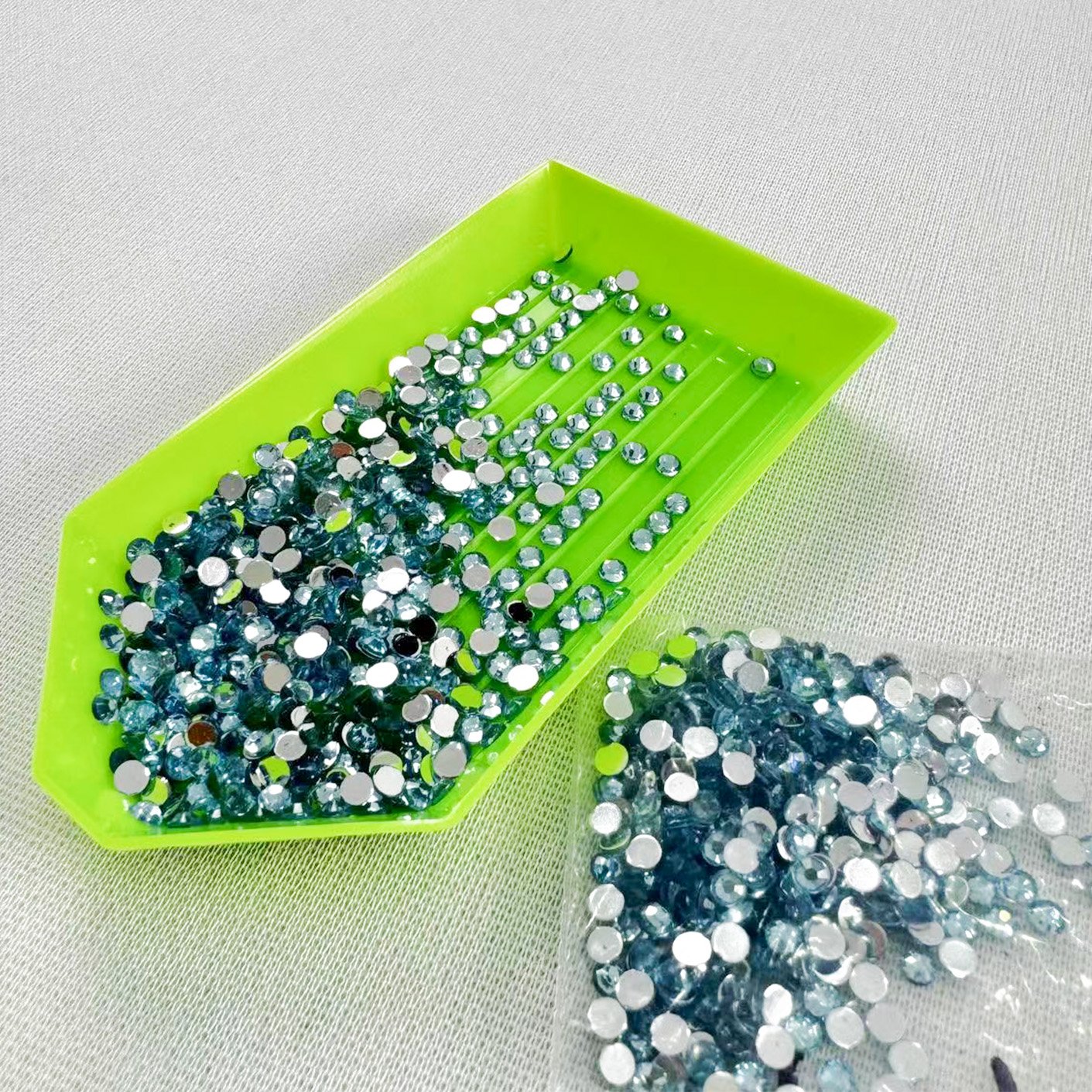 Diamond art kit blue crystals in a green sorting tray and plastic bag on a white textured surface