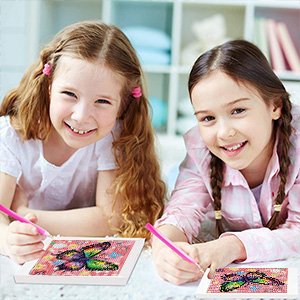 Two smiling girls doing diamond art kits with butterfly designs, holding painting pens