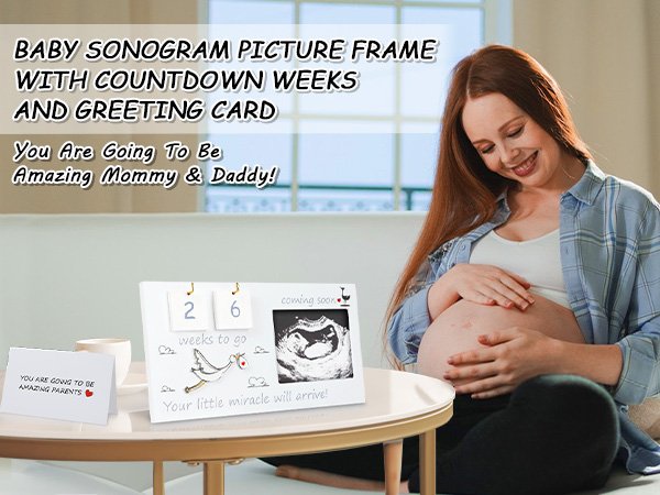 Pregnant woman smiling, holding her belly, with a baby sonogram picture frame and greeting card on a table.