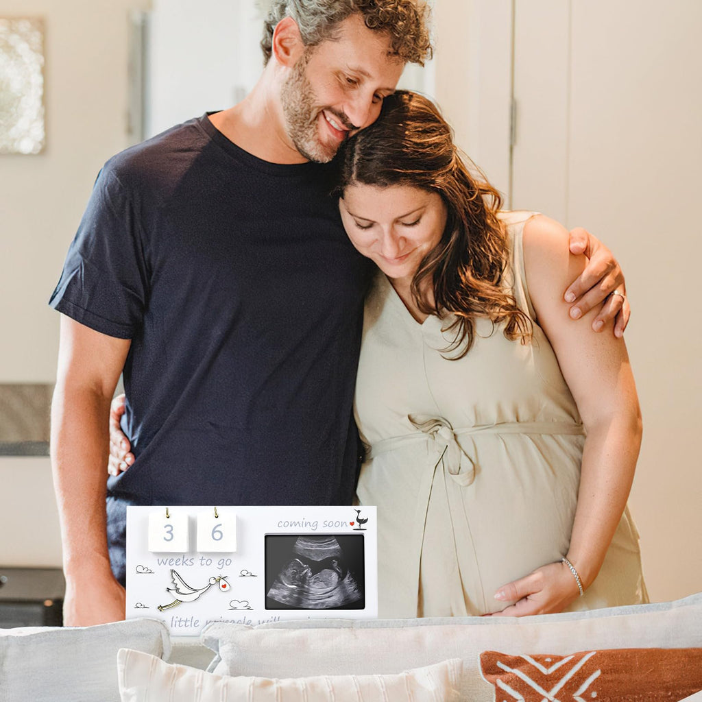 Couple holding each other, displaying a baby sonogram picture frame with countdown.