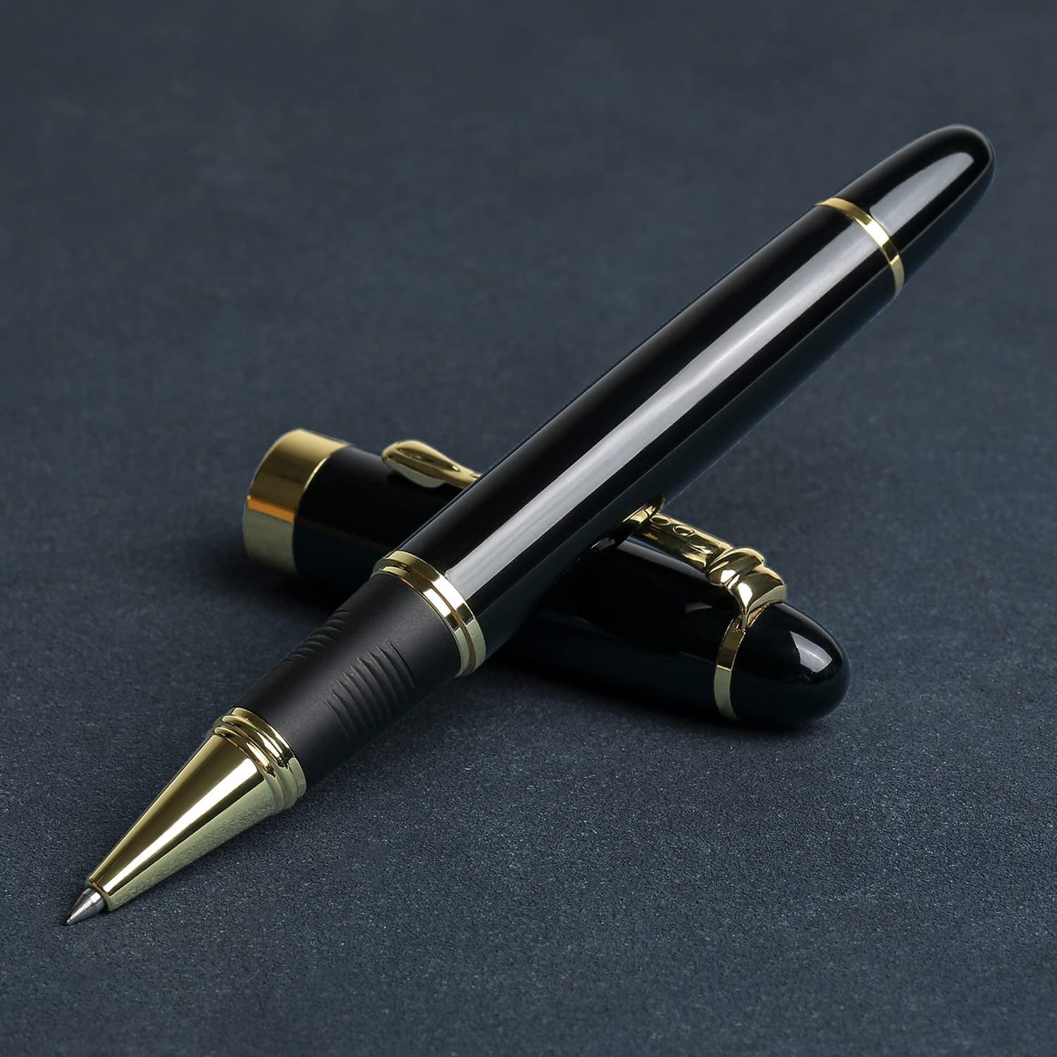 Black and gold ballpoint pen with cap resting beside it on a dark textured surface.