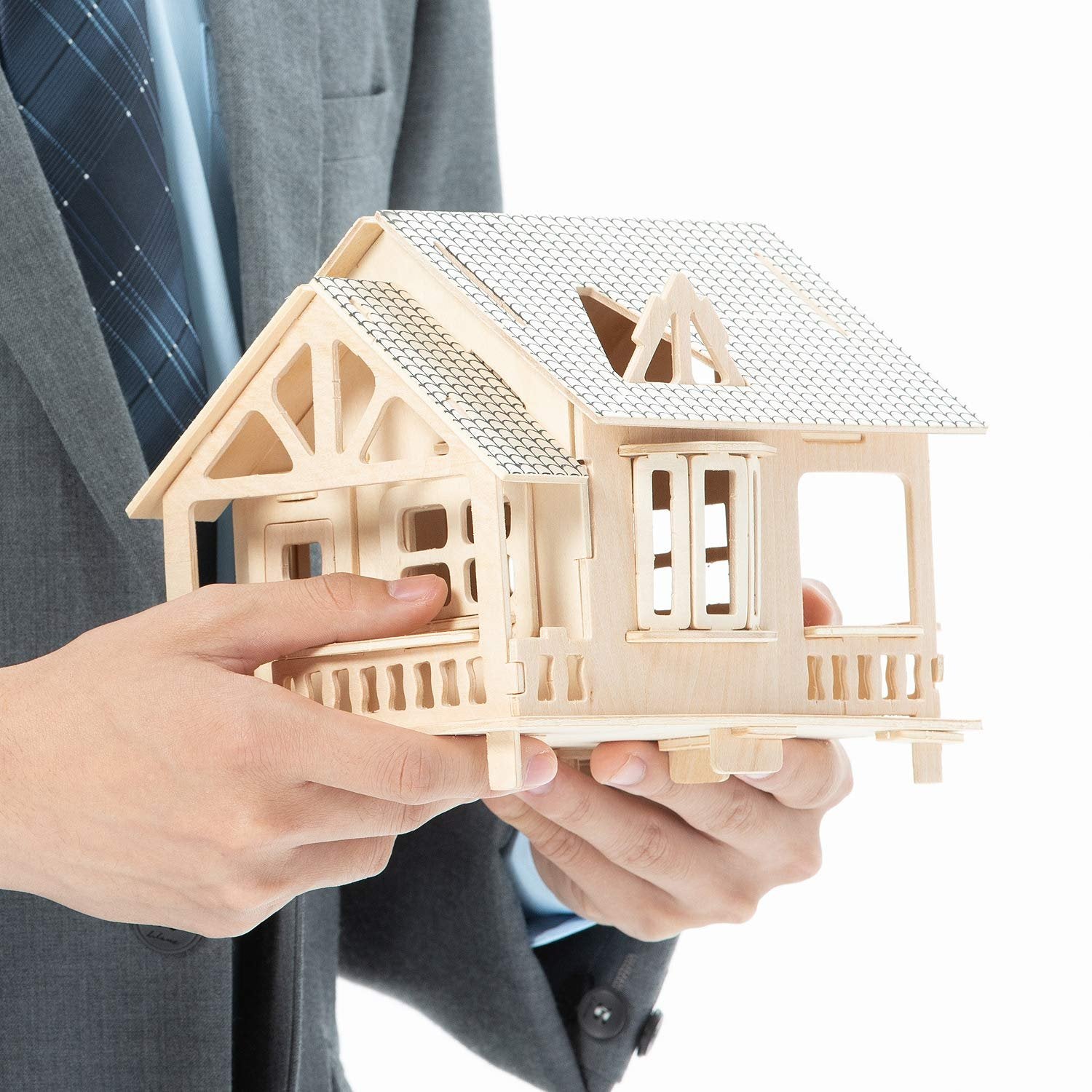 Man in suit holding a wooden model house with intricate details and a patterned roof.