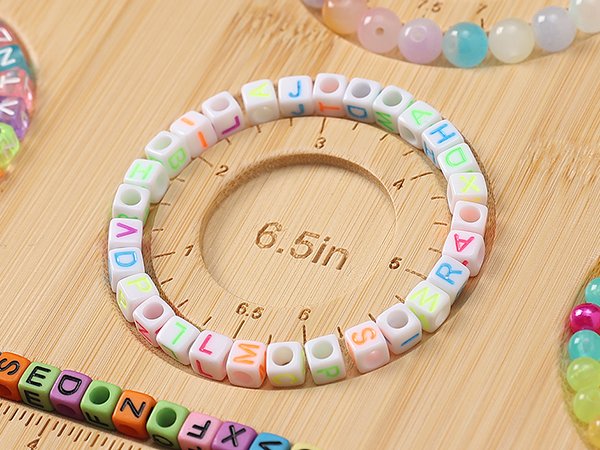Close-up of a bamboo bead board with ruler markings, showing colorful letter beads forming bracelets and other beads.
