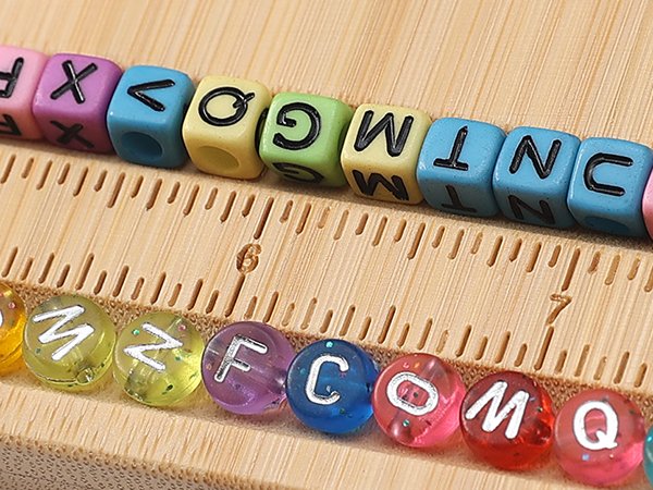 Close-up of colorful letter beads and round beads arranged on a bamboo jewelry making board with ruler markings.