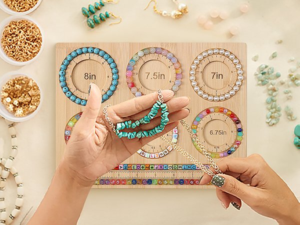 Hands holding a turquoise beaded necklace over a bamboo jewelry making board with bracelet size grooves and bead storage slots.
