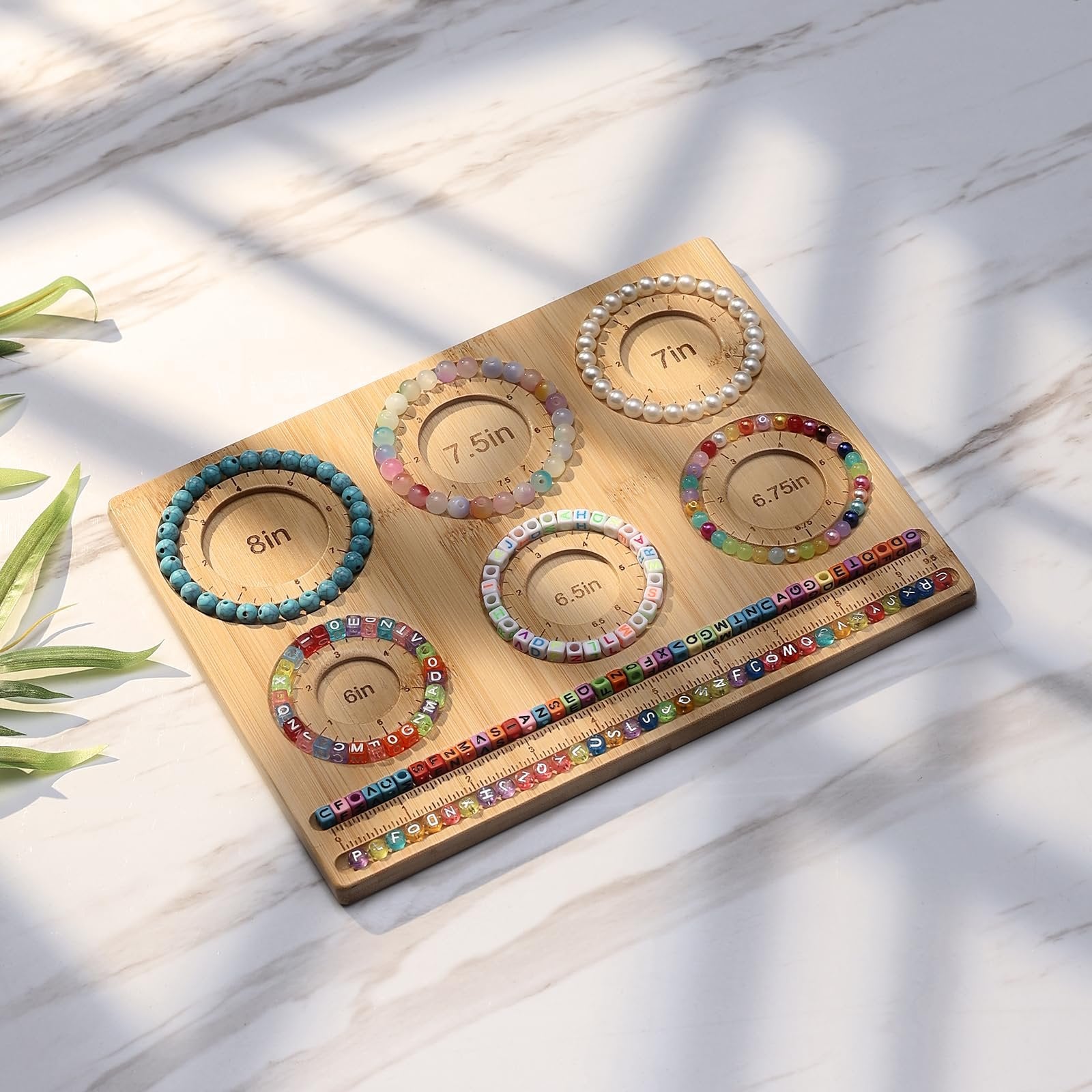 Bamboo jewelry making board with bracelets and beads laid out, showing size guides.
