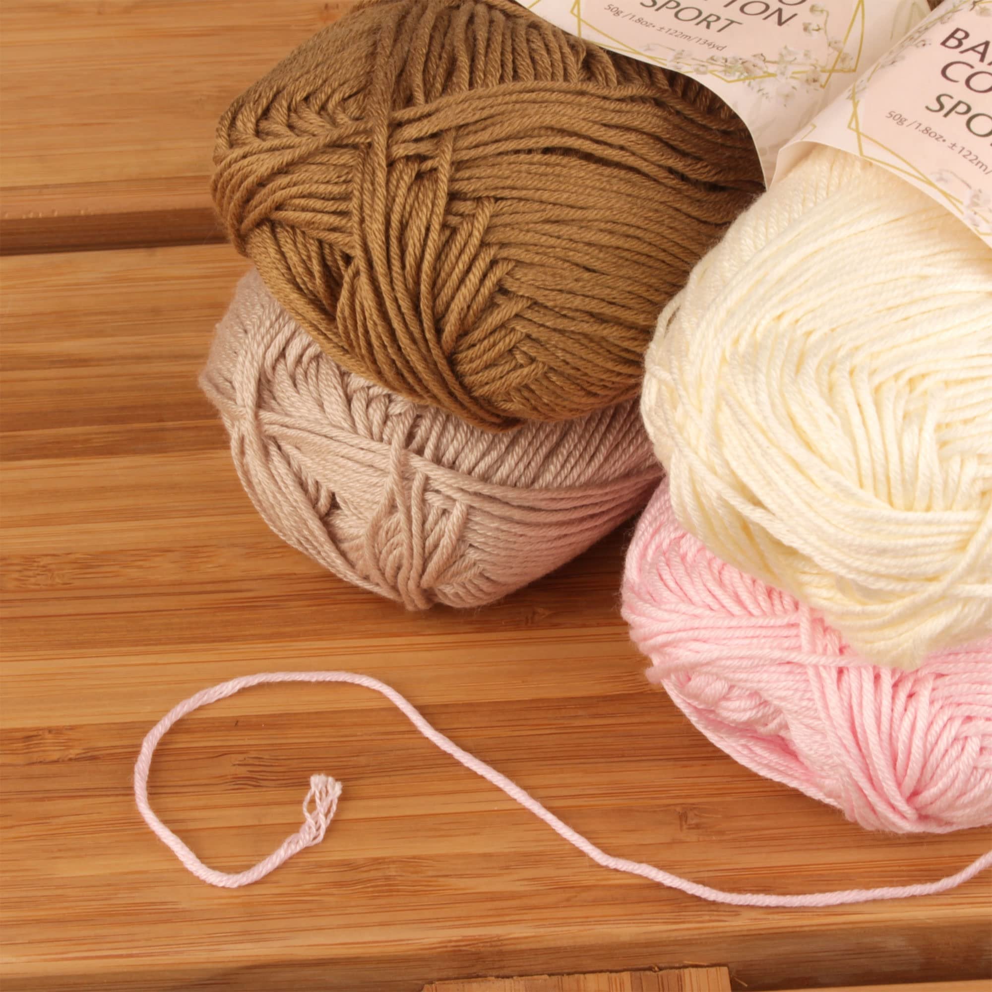 Four skeins of sport yarn in neutral tones, with a loose strand of pink yarn in the foreground on a wooden surface.