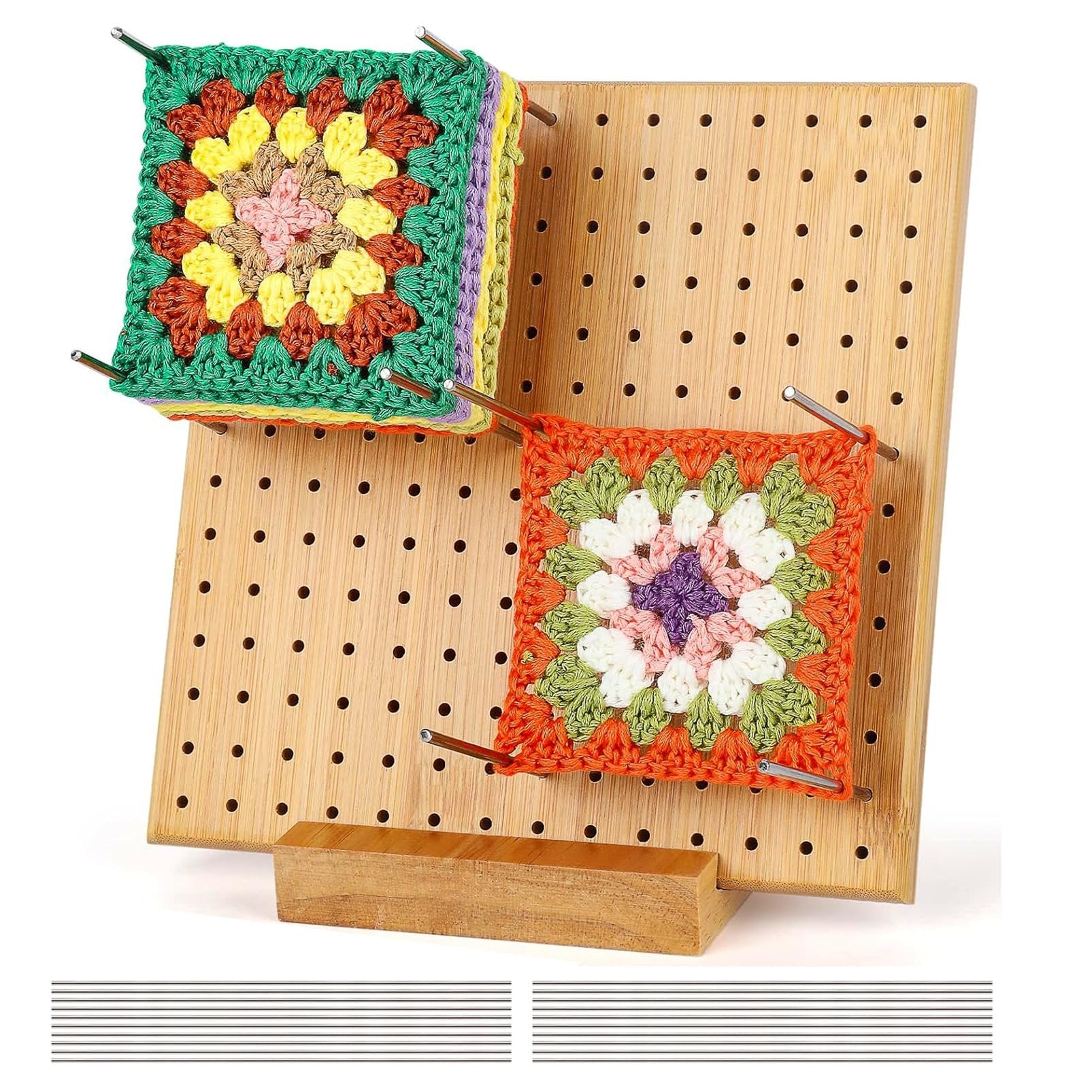 Bamboo crochet blocking board with two colorful granny squares attached by stainless steel pegs, shown at an angle with a wooden base and extra pegs below.