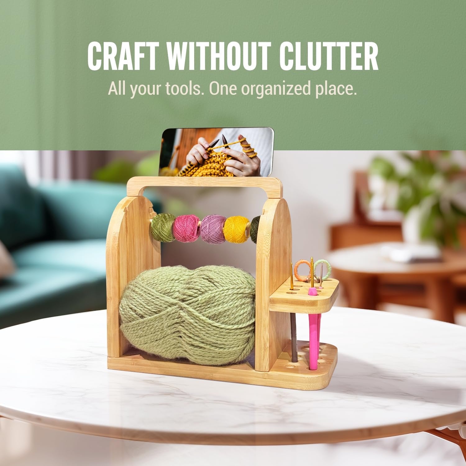 Bamboo yarn organizer with large green yarn ball and smaller colorful yarn balls on dual rods, plus crochet hooks and scissors on a side tray.