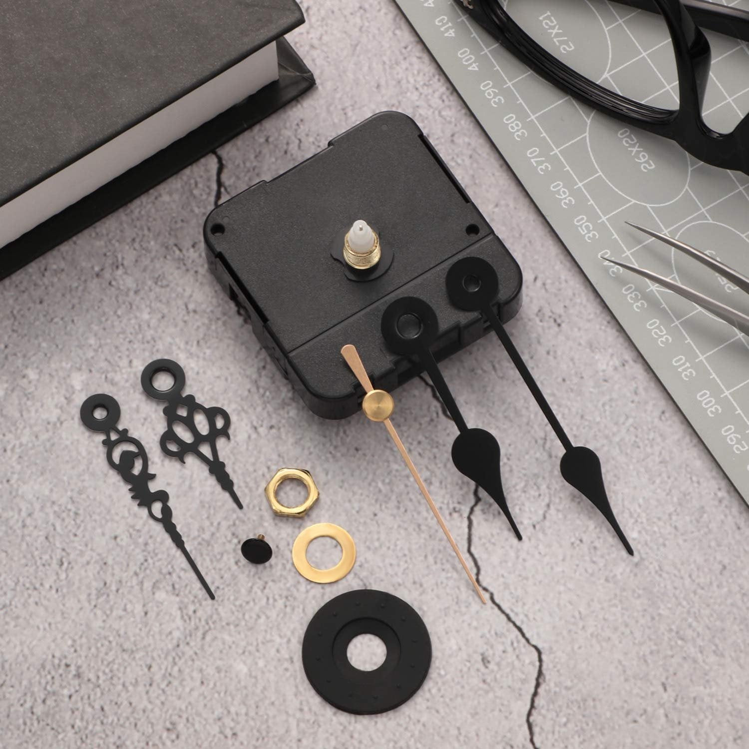 Quartz clock movement mechanism kit with hands, nuts, and washers on a textured surface next to a book and ruler.