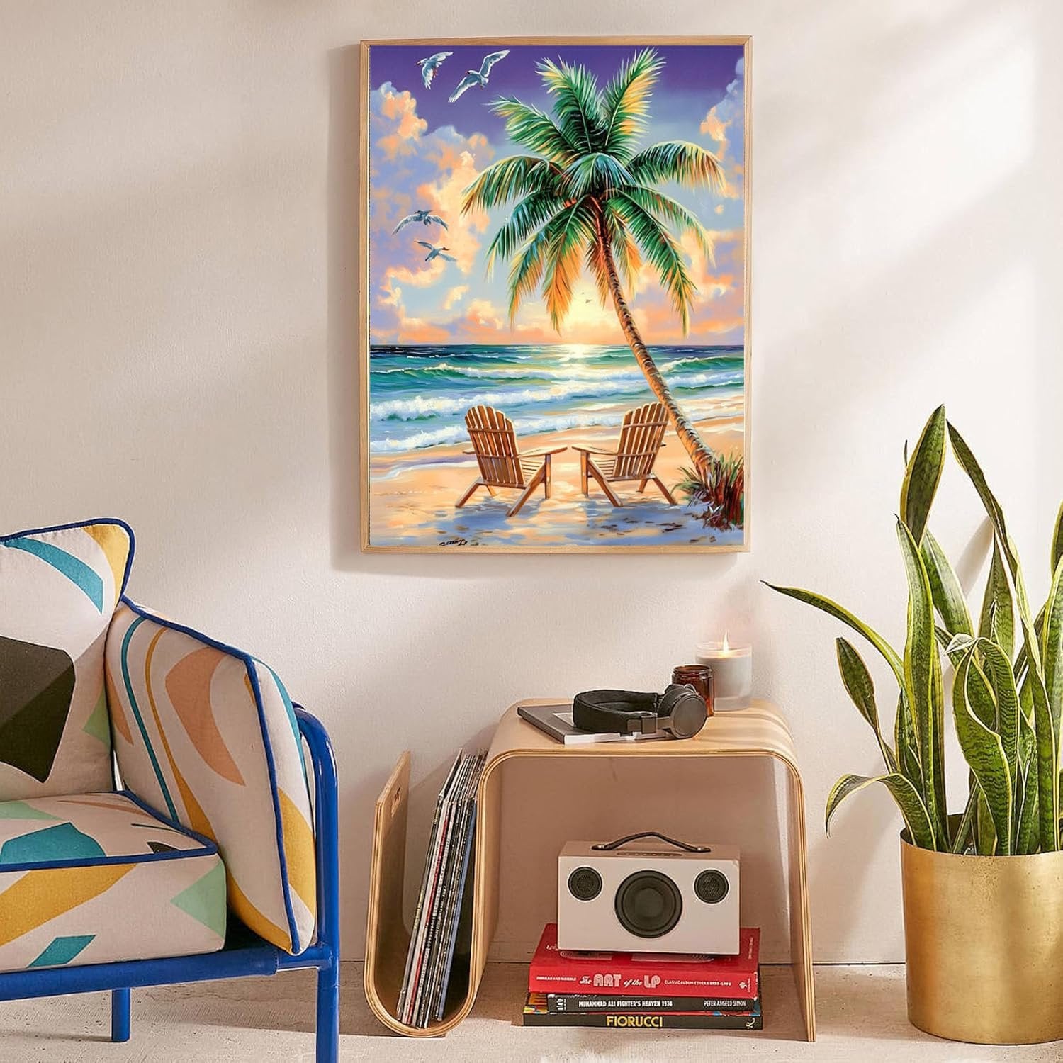 Framed beach diamond painting with palm tree and chairs hanging on wall above side table.